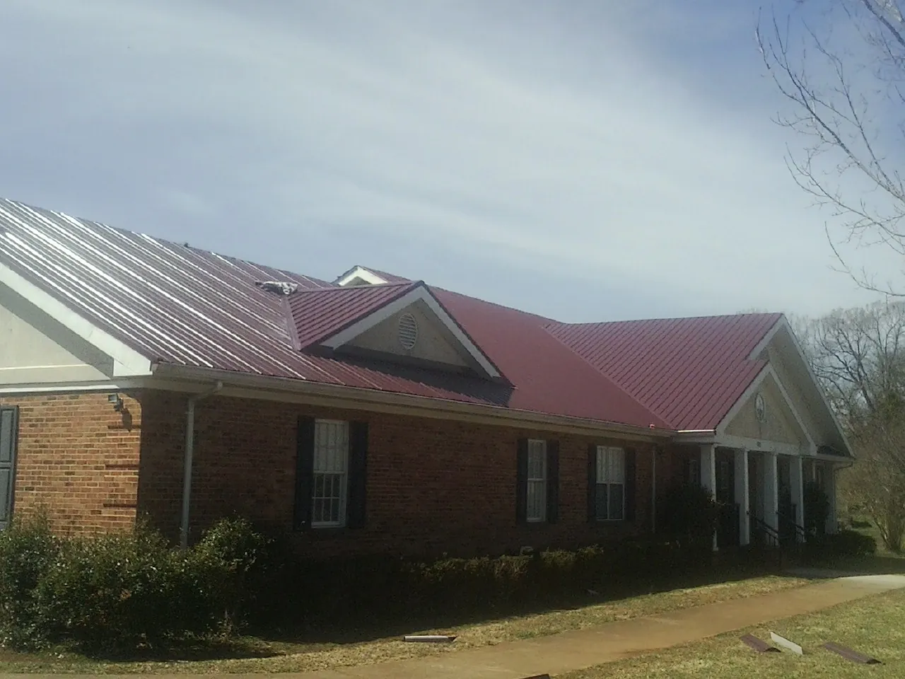 Red metal roof with gabled entries on a long brick building, from a Hail Damage Roof Repair job in Swampscott