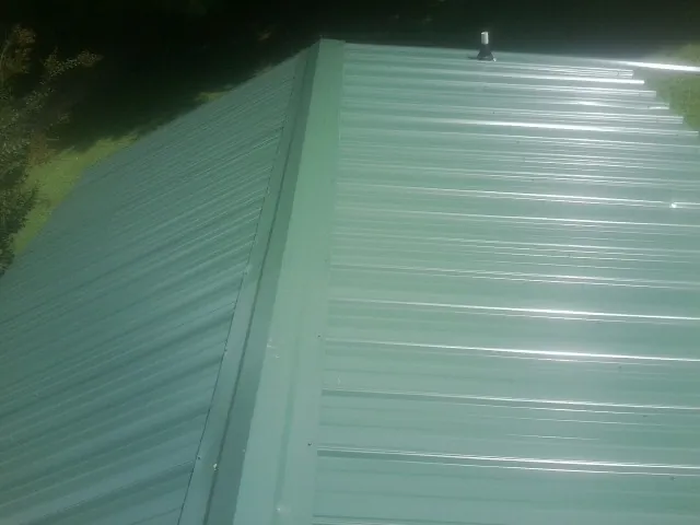New green metal panels meeting at the ridge of a roof — Flat Roof Repair work by our crew in Swampscott