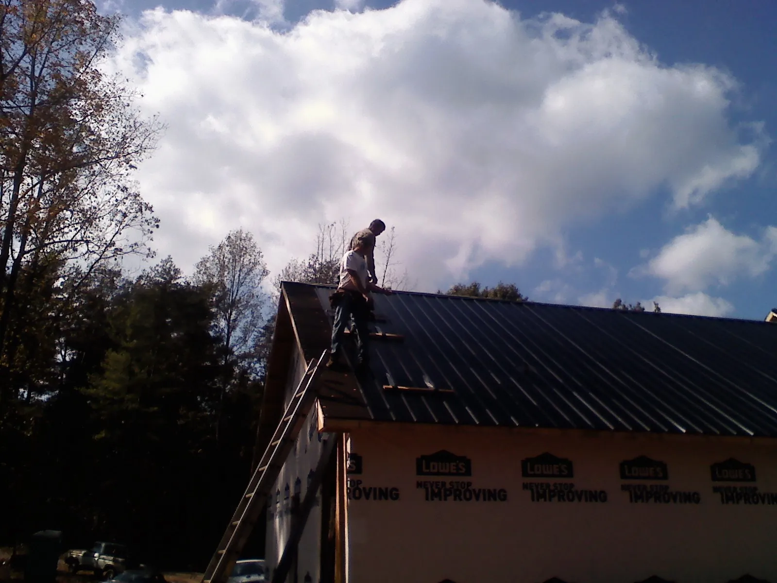 Roofer fastening dark metal panels high against a cloudy sky, from a Roof Inspection job in Swampscott