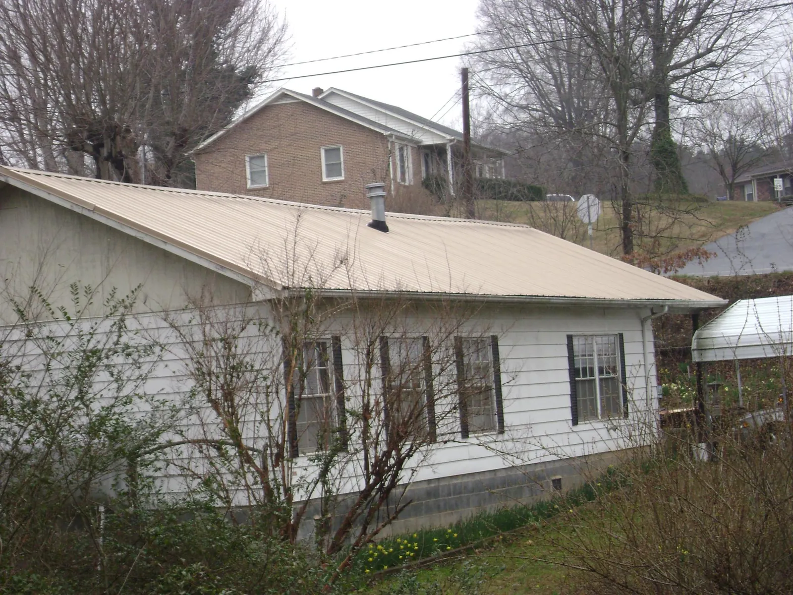 Tan metal roof on a white sided house set into a hillside — Commercial Roofing by Roofing Brothers in Swampscott